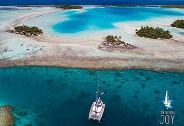 Aerial view of a sailing yacht in turquoise waters near tropical islands and coral reefs in French Polynesia.