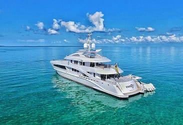 Luxury yacht floating on clear blue ocean near tropical island with partly cloudy sky in the background.