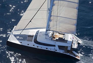 Luxury catamaran sailing on clear blue ocean water under sunlight.