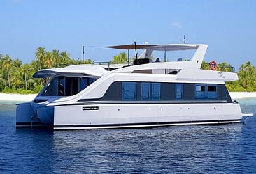 Luxury catamaran yacht near tropical island with palm trees, sailing on calm blue waters under clear sky.