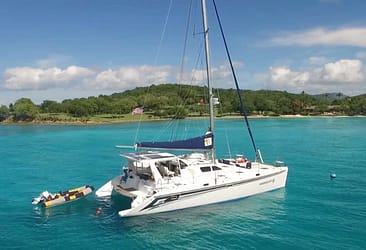 Catamaran anchored in clear turquoise waters near a lush tropical island under a sunny blue sky.