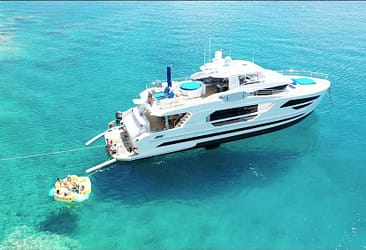 Luxury yacht anchored in clear turquoise waters with people enjoying a floating platform nearby, showcasing a serene marine leisure scene.