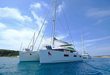 Luxury catamaran sailing on clear blue waters with a scenic coastline in the background.