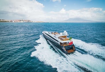 Luxury yacht sailing near the coast of Naples with Mount Vesuvius in the background on a clear day.