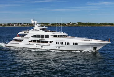 Luxury yacht Aspen Alternative cruising on open water with coastal houses in the background on a clear day.