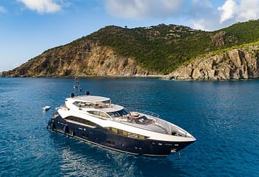 Luxury yacht cruising in clear blue waters near a scenic mountainous coastline.