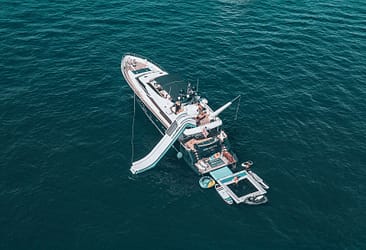 Luxury yacht with inflatable slide and recreational water toys floating on open sea.