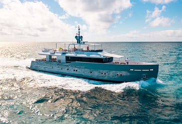 Luxury yacht cruising on open sea under blue sky, showcasing modern design and sleek exterior on a sunny day.
