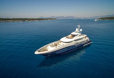 Luxury yacht cruising in the open sea with clear blue water, near a distant shoreline under a clear sky.