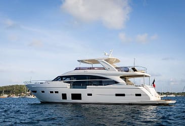 Luxury white yacht sailing on calm blue waters under a clear sky, surrounded by distant boats and a scenic coastline.
