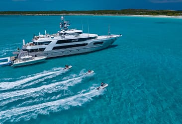 Luxurious yacht anchored in clear blue waters with three jet skis cruising alongside, offering a perfect tropical getaway experience.