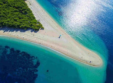 Aerial view of Zlatni Rat beach on Brac Island, Croatia, featuring a distinctive V-shaped sandy shoreline surrounded by clear turquoise waters and lush green forests.