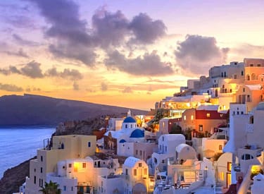 Sunset view of Santorini's iconic whitewashed buildings and blue domes overlooking the Aegean Sea, Greece.