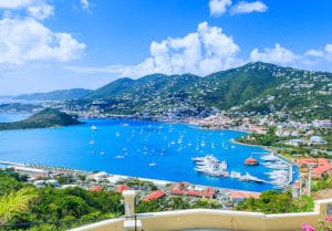 Panoramic view of tropical harbor with sailboats and lush green hills in the Caribbean, under a clear blue sky.