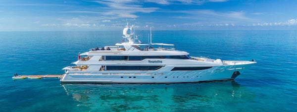 Luxury yacht cruising on tranquil blue ocean under clear sky, showcasing sleek design and spacious decks.