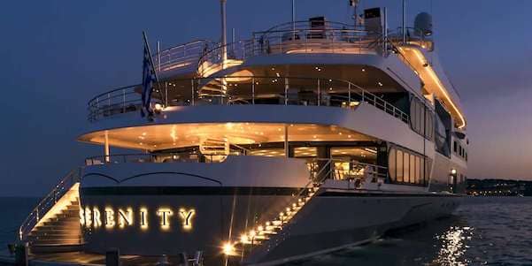 Luxurious yacht named Serenity illuminated at night on the water, showcasing elegant design and opulent lighting against a twilight sky.