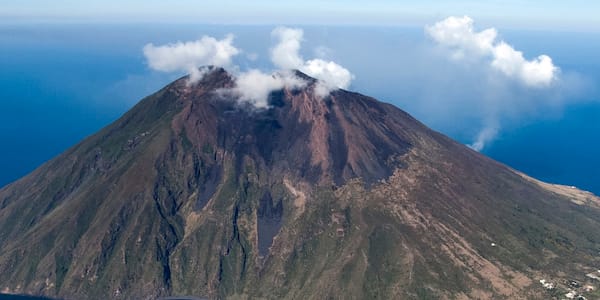 Aerial view of Stromboli volcano with plume of smoke rising, situated in the Aeolian Islands, Italy, surrounded by the blue Mediterranean Sea.