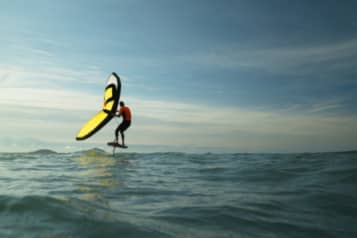 Person engaged in wing foiling on ocean waves under a clear sky.