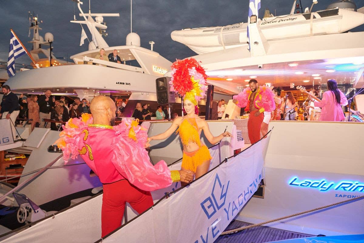 Dancers in colorful costumes perform on a luxury yacht during an evening event, surrounded by an enthusiastic crowd.