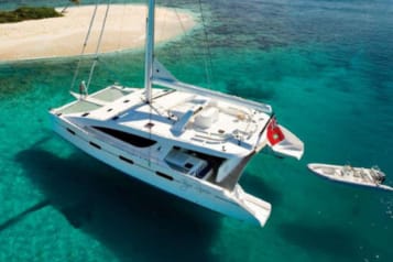 Luxury catamaran sailing near a tropical island with crystal clear water and sandy beach, ideal for vacation and adventure enthusiasts.