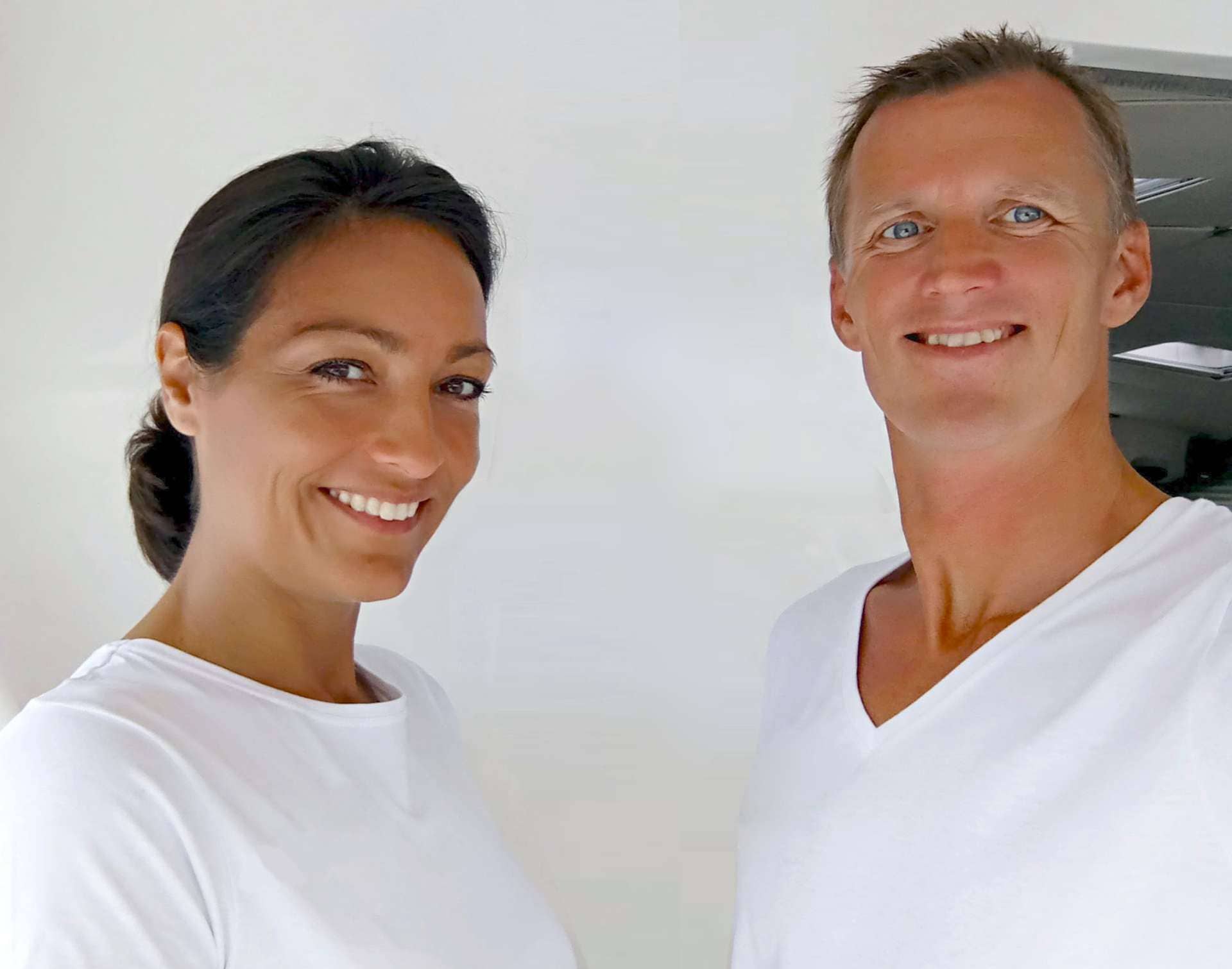Smiling man and woman in white shirts standing in a bright room.