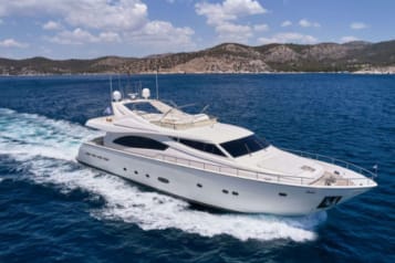 Luxury yacht cruising on clear blue waters with mountainous coastline in the background.