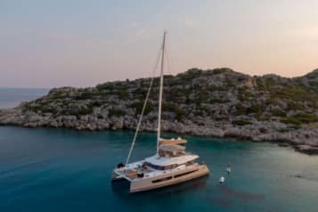 Luxury sailboat anchored in tranquil turquoise waters near a rocky island coastline during sunset.