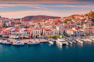 Scenic view of Poros, Greece with vibrant buildings and docked yachts along the waterfront at sunset.