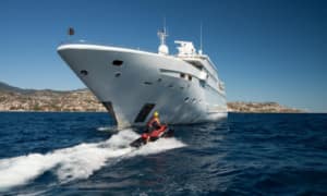 Luxury yacht sailing near the coast with person riding a jet ski in the foreground on a sunny day.