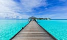 Tropical wooden pier leading to gazebo over turquoise ocean with clear blue sky.