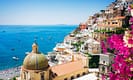 Scenic view of Positano on the Amalfi Coast, featuring colorful cliffside buildings, vibrant bougainvillea, and boats dotting the turquoise sea.