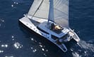 Luxury sailing catamaran cruising in clear blue ocean waters with sun reflecting on the surface, showcasing elegant design and spacious deck.