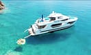 Luxury yacht anchored in clear turquoise waters with people enjoying a floating platform nearby, showcasing a serene marine leisure scene.