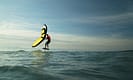 Person engaged in wing foiling on ocean waves under a clear sky.