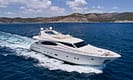Luxury yacht cruising on clear blue waters with mountainous coastline in the background.