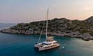 Luxury sailboat anchored in tranquil turquoise waters near a rocky island coastline during sunset.