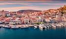 Scenic view of Poros, Greece with vibrant buildings and docked yachts along the waterfront at sunset.